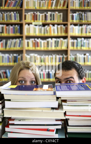 Les étudiants, paire, à la recherche de derrière des piles de livres, la bibliothèque de l'université Banque D'Images