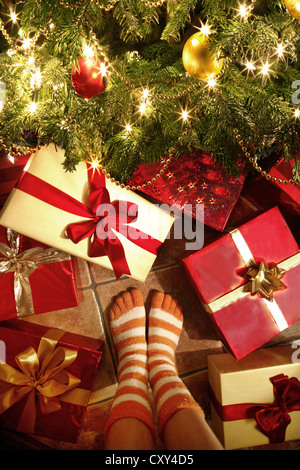 Fille, vue de détail, les jambes, debout devant des cadeaux de Noël sous un arbre de Noël Banque D'Images