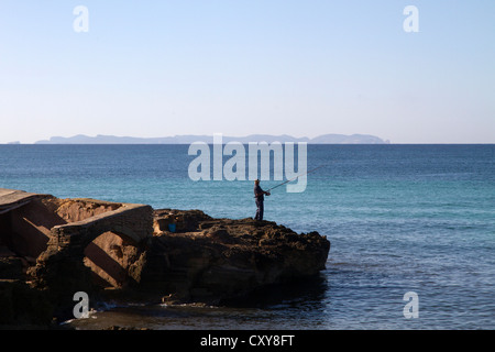 L'homme pêche en mer Méditerranée par l'eau de roche, l'île de Cabrera sur fond d'horizon, Majorque Îles Baléares Espagne Banque D'Images
