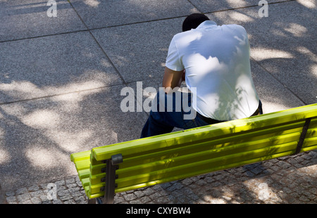 Avec l'homme s'inclina la tête assis sur un banc de parc vert, Berlin Banque D'Images