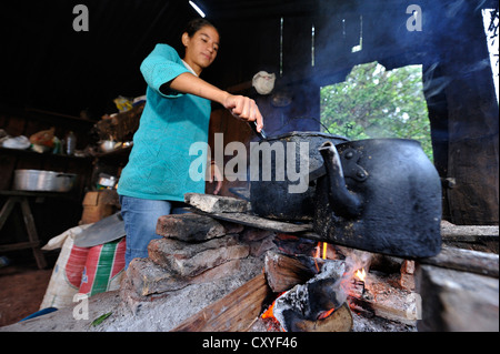 Jeune femme la cuisson sur un feu ouvert dans la cuisine simple des travailleurs agricoles, Comunidad Arroyito, Concepcion Banque D'Images