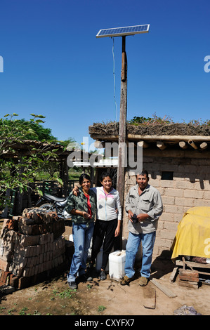 Famille d'agriculteurs debout devant leur hutte avec une cellule solaire, Gran Chaco, Province de Santiago del Estero, Argentine Banque D'Images