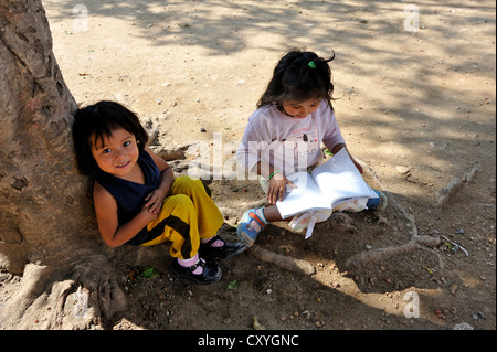 Deux filles avec les livres d'exercice assis dans l'ombre d'un arbre, Lomas de Santa Faz slum, Guatemala City, Guatemala Banque D'Images