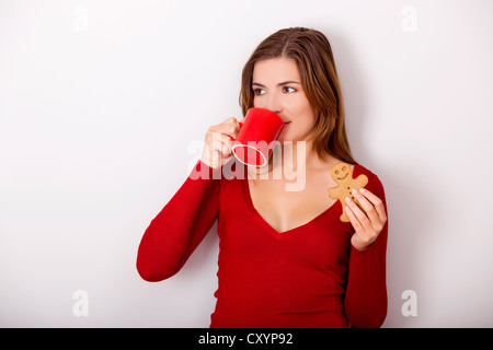 Belle Femme buvant un café chaud et de manger a gingerbread cookie, contre un mur gris Banque D'Images