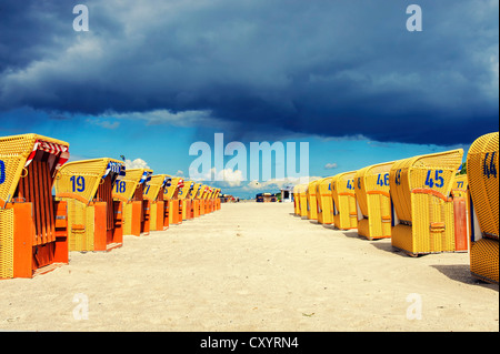 Deux rangées de chaises de plage en osier couvert jaune au soleil, sombres nuages de pluie à l'arrière, Mecklembourg-Poméranie-Occidentale Banque D'Images