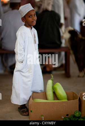 En Dishdasha garçon debout à côté d'une boîte de légumes, de Sinaw, Oman Banque D'Images