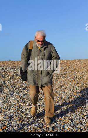 Personnes âgées homme marchant avec précaution sur une plage de galets Banque D'Images