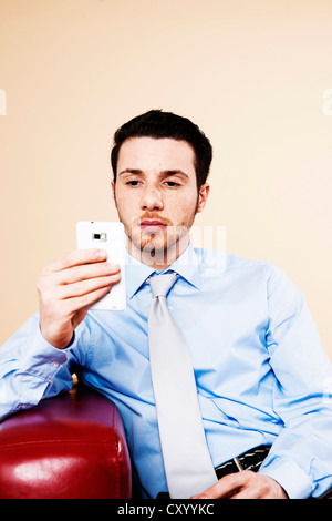 Jeune manager assis sur un canapé avec son smartphone et la vérification d'un SMS Banque D'Images