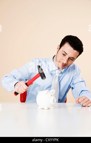 Jeune homme sur le point de frapper une tirelire avec un marteau Banque D'Images