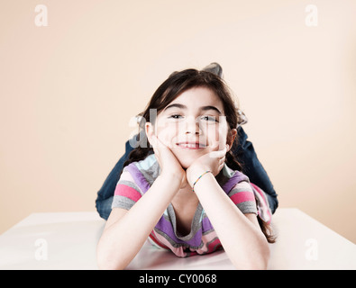 Smiling girl couchée sur le ventre avec sa tête reposant dans ses mains Banque D'Images