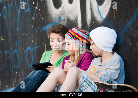 Trois ados avec un tablet PC assis devant un mur de graffiti Banque D'Images