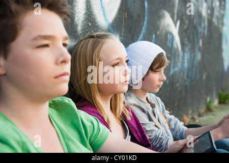 Trois adolescents assis devant un mur de graffiti Banque D'Images