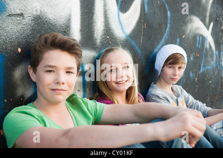 Trois adolescents assis devant un mur de graffiti Banque D'Images