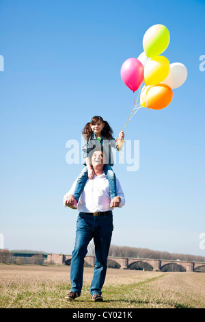 Girl holding de nombreux ballons colorés dans sa main alors qu'il était assis sur les épaules de son grand-père Banque D'Images