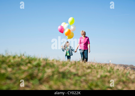 Girls holding balloons dans sa main tout en marchant avec sa mère dans un pré Banque D'Images