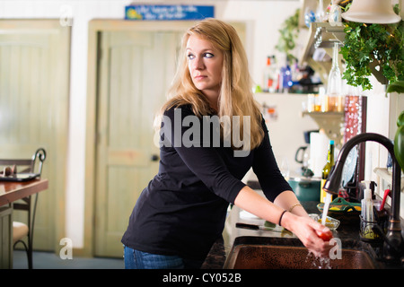 Femme au foyer, 35 ans, de race blanche, à la recherche de légumes pendant le lavage suspectes dans son évier de cuisine Banque D'Images