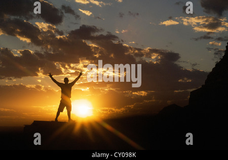 La figure masculine with arms outstretched standing avec coucher du soleil en arrière-plan Banque D'Images