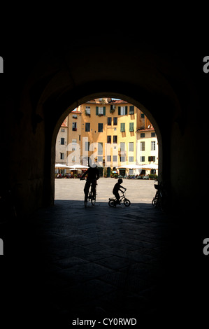 Vélo adulte et enfant dans l'ombre sur une piazza en Italie tourné à travers un passage voûté Banque D'Images