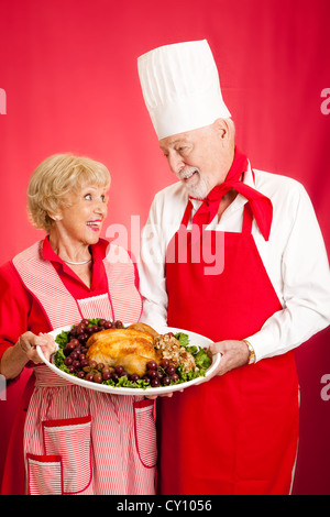 Chef et femme au foyer ont collaboré à faire un délicieux dîner à la dinde. Fond rouge. Banque D'Images