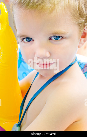 Close-up of a beautiful cinq ans garçon autiste jouant dans une pataugeoire avec un canard jaune flottant. Banque D'Images