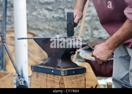 Maréchal-ferrant avec marteau dans le motion blur smashes avec pleine force active à une tige de fer rouge sur la pièce d'une enclume de forgeron Banque D'Images