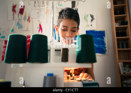 Les petites entreprises et les travailleuses autonomes, young hispanic woman travaillant comme styliste de mode avec machine à coudre dans studio Banque D'Images