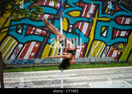 Un danseur effectue une pose sur un poteau en plein air à côté d'un graffiti urbain. Banque D'Images