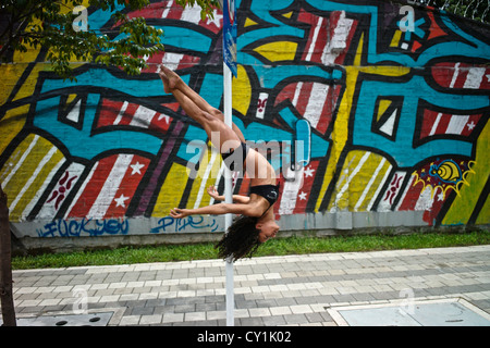 Un danseur effectue une pose sur un poteau en plein air à côté d'un graffiti urbain.