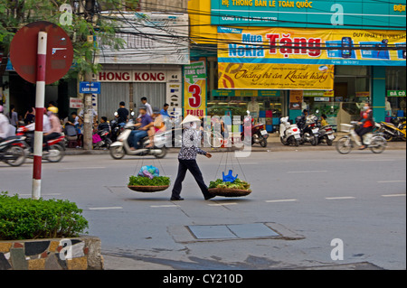 Une dame vietnamienne marchant le long d'une rue animée road avec ses paniers de légumes à Hai Phong Vietnam Banque D'Images