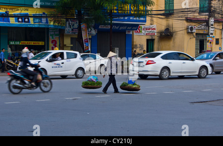 Une dame vietnamienne à marcher le long d'une route très fréquentée avec ses paniers de légumes à Hai Phong Vietnam Banque D'Images