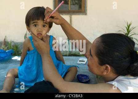 Une jeune fille apparaît résigné à avoir ses sourcils peints par sa mère. Lombok, Indonésie Banque D'Images