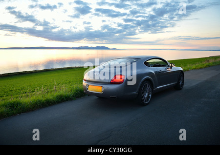 Bentley Continental GT à côté de la plage et de la mer au coucher du soleil et des îles dans l'arrière-plan et nuages dans le ciel Banque D'Images