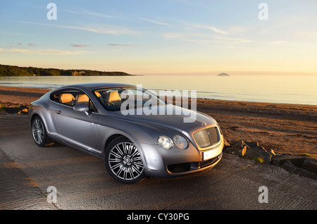 Bentley Continental GT à côté de la plage et de la mer au coucher du soleil et des îles dans l'arrière-plan et nuages dans le ciel Banque D'Images