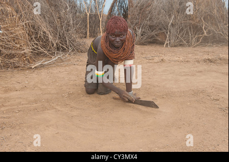 Les Nyangatom (Bumi) une femme sur ses genoux raclant le sol avec une machette, vallée de la rivière Omo, en Ethiopie Banque D'Images