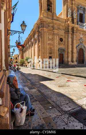 Vieille Femme se reposer en face de la cathédrale San Tomaso di Canterbury, Marsala, Sicile, Italie Banque D'Images