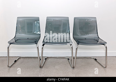 Trois gris transparent plastique et métallique chaises dans une rangée Banque D'Images
