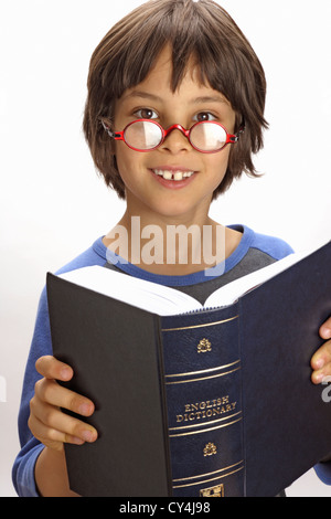 Garçon de huit ans avec des lunettes de sourire et de dictionnaire d'ouverture Banque D'Images