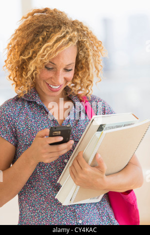 USA, New Jersey, Jersey City, jeune femme portant des livres et à l'aide de mobile phone Banque D'Images