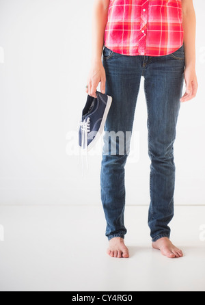 Studio shot of young woman holding barefoot shoes, low section Banque D'Images