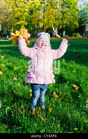 La petite fille recueille les feuilles tombées en automne park Banque D'Images