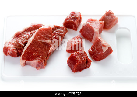 La jambe d'agneau cru steaks et les dés d'agneau sur une planche à découper sur blanc Banque D'Images