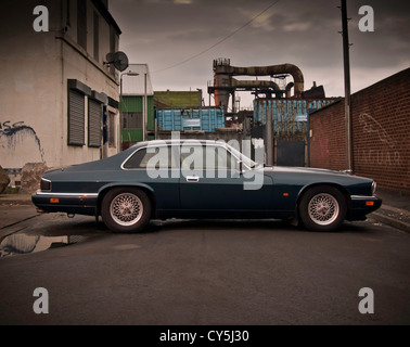 Classic Sports voiture garée dans une rue avec tuyauterie industrielle dans l'arrière-plan et Jaguar graffiti sur mur de briques. Banque D'Images