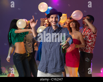 Jeune homme s'amuser à partie, tenant un verre, avec des amis derrière, jouer avec des ballons et des bulles Banque D'Images