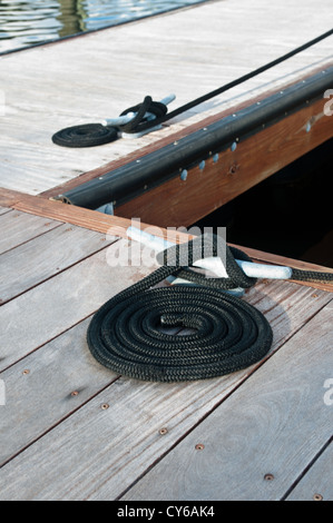 Cordes Noir enroulé sur un quai en bois et liés à un dock metal tasseaux. Tasseaux sont utilisés pour sécuriser les docks et les lignes de bateaux Banque D'Images