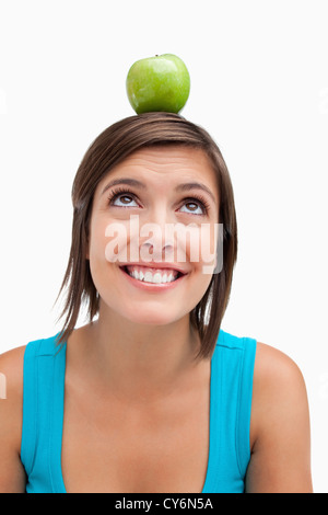 Smiling teenage girl essaie de regarder une pomme placée sur la tête. Banque D'Images