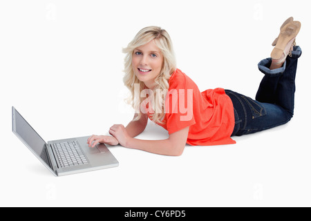 Smiling blonde woman crossing ses jambes devant son ordinateur portable Banque D'Images