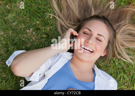 Jeune fille riant couchée sur le dos tout en parlant au téléphone Banque D'Images