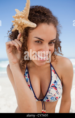 Jeune femme se penchant la tête en avant tout en tenant une étoile de mer Banque D'Images