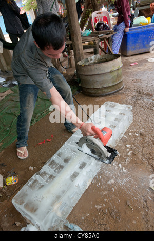 Un marchand de glace utilise une scie circulaire pour diviser un gros bloc de glace dans la région de O'Ambel marché, Sisophon, Cambodge Banque D'Images