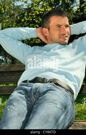 Homme séduisant est reposant sur un banc dans un environnement naturel Banque D'Images
